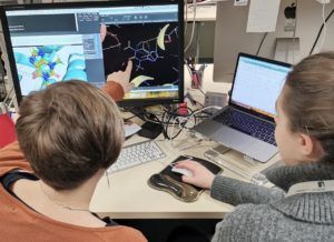 two women working at a computer displaying an image of a chemical fragment attached to a protein