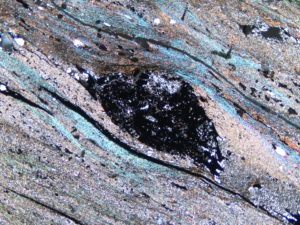 Photo of a thin slice of Cryogenian glacial rock under the microscope. Picture shows pebble which has been squeezed and stretched as the ice moved over it, and beautiful bright colours of the minerals surrounding the pebble