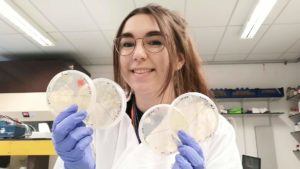 Katie, holding up some agar plates filled with bacterial colonies