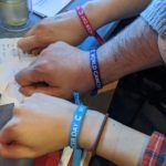 3 people's wrists with wristbands in different colours saying "world cancer day"